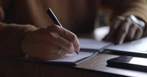 Close up of male hands taking notes in notebook. Backlit, close-up, slow motion Video stock 165629543