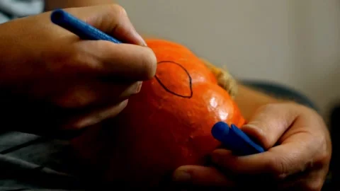 Close-up of male hands using a knife to cut a scary face out of a pumpkin for Video stock 272459274