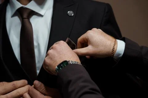 Close-Up of a Man Adjusting His Brown Tie and Pocket Square in a Black Suit.. Stock Photos
