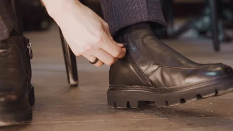 Close up of man adjusting zipper on his black leather ankle boot featuring shoe Stock Footage 344871412