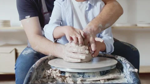 Close up of man and his son are making pot from clay on throwing wheel in studio Stock Footage 143615672