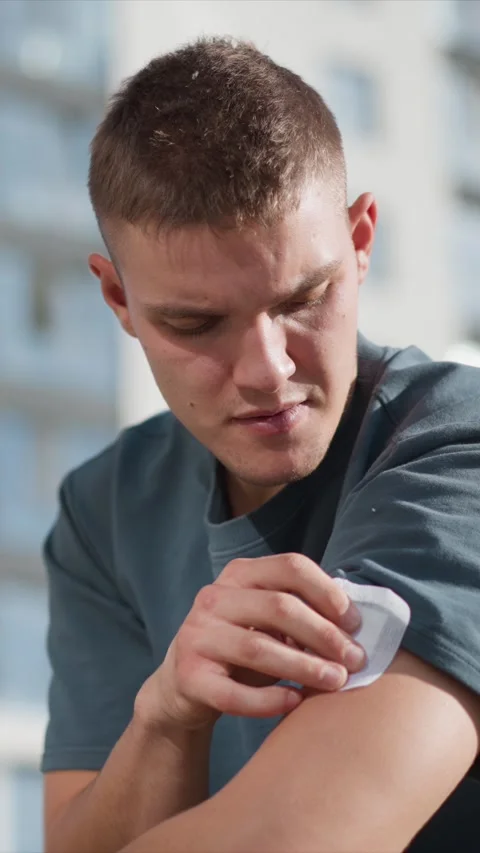 Close up of man applying adhesive bandage to arm in bright outdoor setting with Stock Footage 345073789