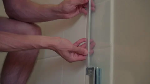 Close-up man applying water seal strip to glass shower door Stock Footage 286374692