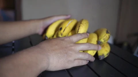 Close-up of a man arranging fresh yellow Ambon bananas on a black table indoors Stock-Footage 321423716
