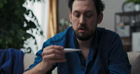 Close-up of man with beard and dark hair who is sick. Man in blue pajamas holds 스톡 동영상 218318307