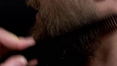 Close-up of a man with a beard combing his beard with a comb on a black Stock Footage 144641227
