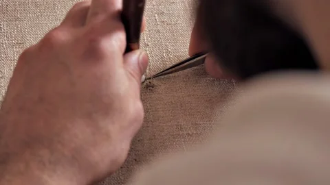 Close-up of a man with a beard restoring a painting canvas after damage Stock Footage 222970543