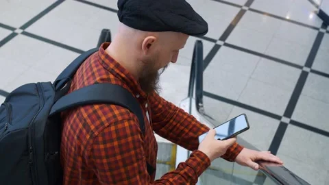 A close-up of a man with a beard walks down the escalator while browsing his Stock Footage 206800821