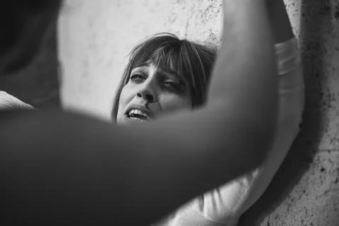 Close-up of a man from behind, hitting with a crying woman to a dirty wall Stock-Fotos
