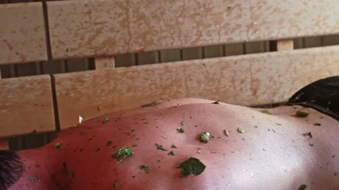 Close-up of a man being beaten on the back steamed with a juniper broom in the Stock Footage 223880929