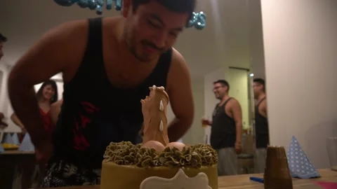 Close-up of a man biting a penis-shaped cake for his friend's happy birthday Stock Footage 194502639