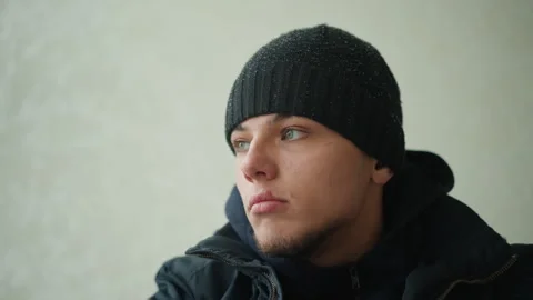 Close up of man in black beanie and dark jacket against plain light colored Stock Footage 346658701