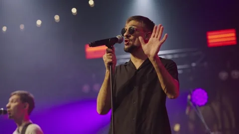 Close-up of man in black glasses performing song at concert into microphone Video stock 243935154
