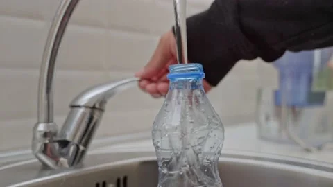 Close-up of a man in a black jacket pouring cold tap water into a plastic bottle Stock Footage 201946289