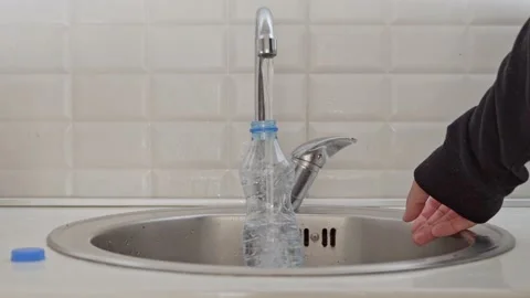 Close-up of a man in a black jacket pouring cold tap water into a plastic bottle Stock Footage 201946360