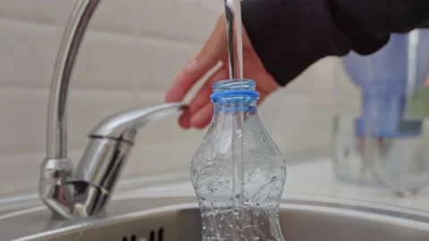 Close-up of a man in a black jacket pouring cold tap water into a plastic bottle Stock Footage 201946443