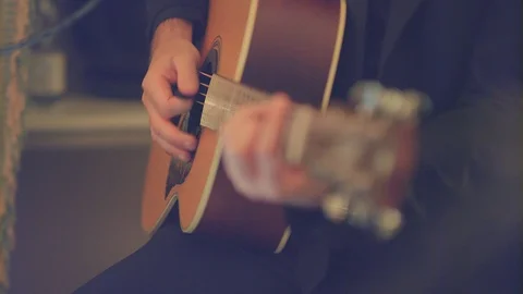 Close-up of a man in a black jacket who plays a brown-yellow acoustic guitar Stock Footage 128428563