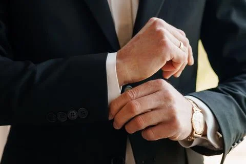 Close up of a man in a black suit adjusting his white shirt cuff while wear.. Stock Photos