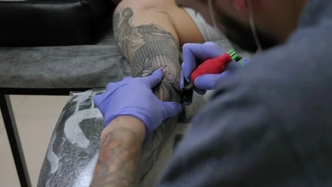 Close-up of a man in blue gloves getting a tattoo on a young woman's arm. Stockbeeldmateriaal 140564040