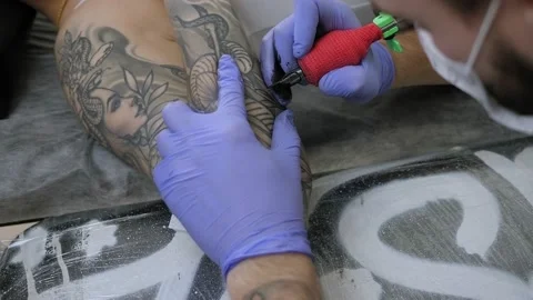 Close-up of a man in blue gloves getting a tattoo on a young woman's arm. Stockbeeldmateriaal 220734295