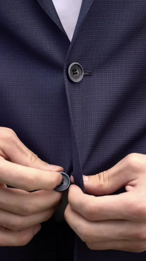 Close-up of a man buttoning a dark navy suit jacket over a white shirt. Stock Footage 344990064