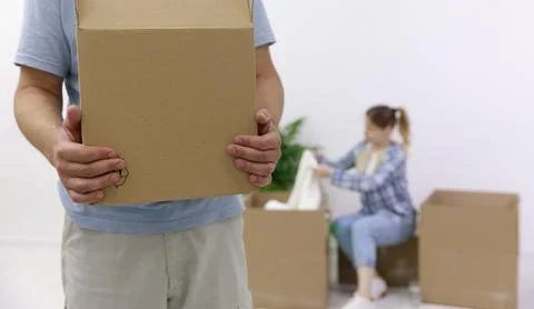 Close-up of a man with cardboard boxes, in the background, a girl unpacks things Foto stock