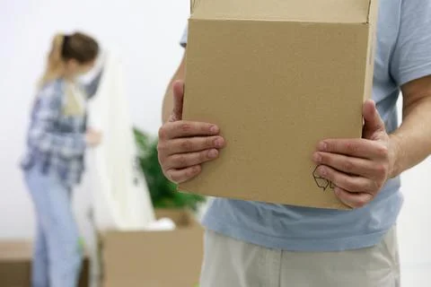 Close-up of a man with cardboard boxes, in the background, a girl unpacks things Stock Photos