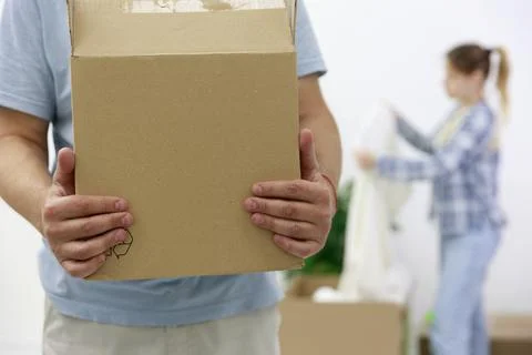 Close-up of a man with cardboard boxes, in the background, a girl unpacks things Foto stock