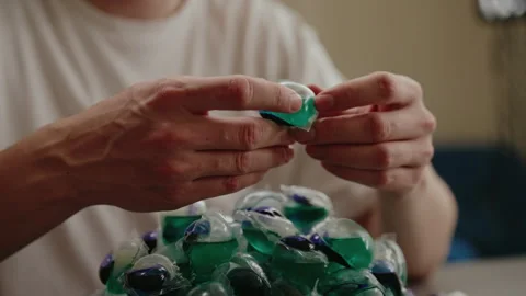 Close-up of man carefully examining laundry detergent pod with pile of similar Stock Footage 313298079