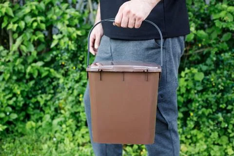 Close-up of a man carrying a brown kitchen compost bin filled with organic wa Stock Photos