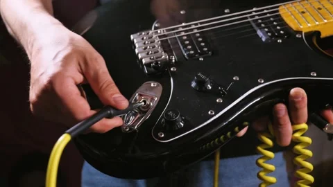 Close-up of a man connecting a yellow cable to a black electric guitar, focusing Video stock 277873606