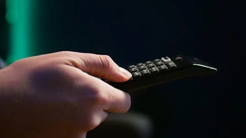 Close up of man on couch using remote control flipping through channels on TV Stock Photos