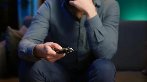 Close up of man on couch using remote control flipping through channels on TV Stock Photos