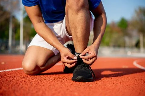 Close up of a man crouching while tying his black sneaker shoelace on racet.. Stock Photos