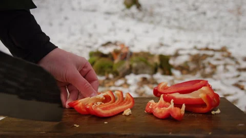 Close up of man cutting fresh red peppers on wooden board near bonfire Stock Footage 308719676