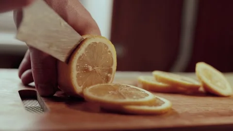 Close up of a man cutting the lemon on a cutting board in kitchen. Lemon juice c Stock Footage 302377989