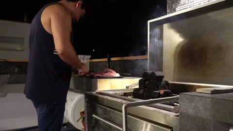 Close-up of a man cutting meats next to a grill with a hexagon-shaped pile of Stock Footage 186223336