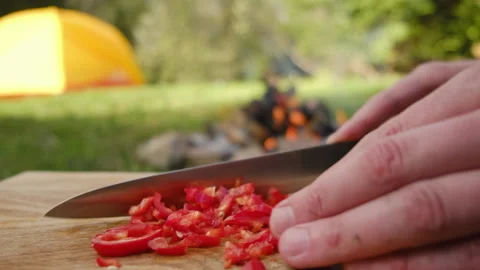 Close up of man cutting pepper on background bonfire, yellow tent Stock Footage 274130187