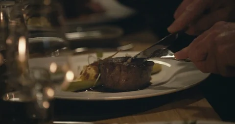 Close up of man cutting slice of steak on plate at restaurant at night Stock Footage 90103696