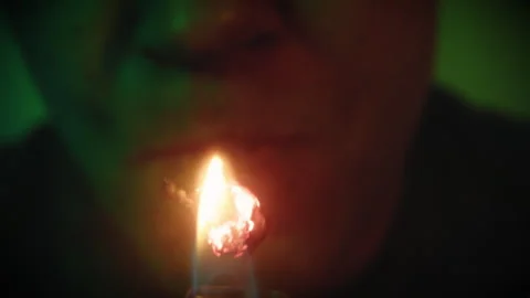Close-up of a man in the dark burns a thick cigarette and exhales the smoke 動画素材 249669025