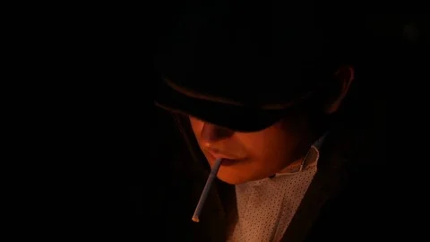 Close-up of a man, detective or thug in a flat cap lights a cigarette from a Vídeos de archivo 119670994