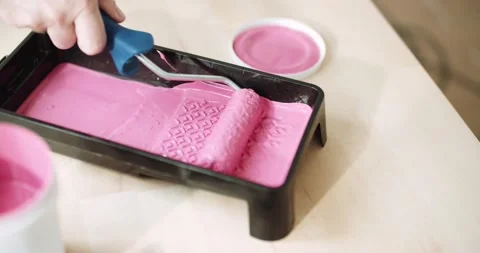 Close-up of a man dipping a roller in a tray of pink paint Stock Footage 155796589