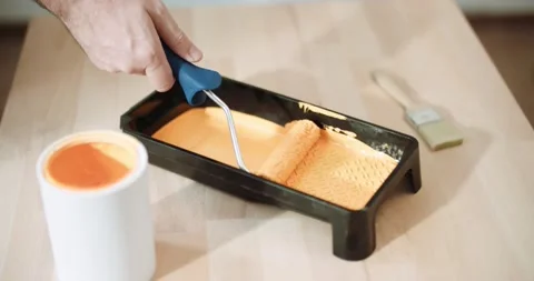 Close-up of a man dipping a roller in a tray of orange paint Stock Footage 155796653
