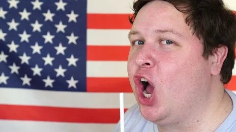 Close-up of a man drinking a cocktail from straw in front of the American Flag Stock Footage 107048796