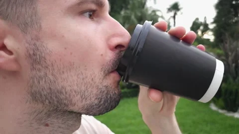 Close-up of man drinking coffee from black takeaway cup outdoors. Video stock 283404160
