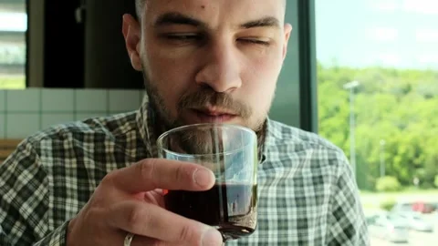 Close-up of a man drinking a dark beverage from a glass in a cafe. He wears a Stock Footage 316142189