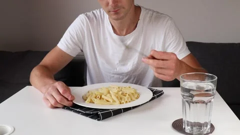 A close-up of a man eating feather pasta, chewing as he sits at a table Stock Footage 281148877