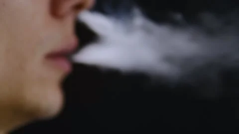 Close-up of a man with an electronic cigarette, exhaling vapor against a black Stock Footage 295779991