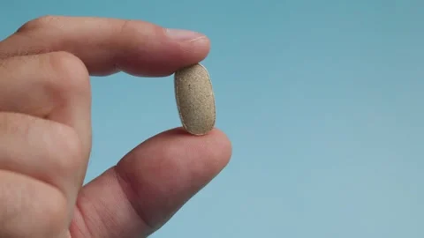 Close up of man fingers holding single medicine capsule on blue back 4k Stock Footage 343450065