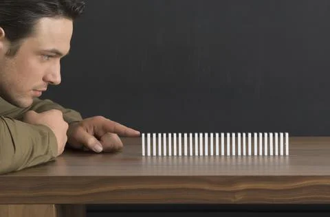 Close-up of a man getting ready to push the first domino in a row of dominoes on Stock Photos